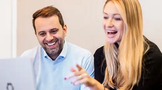 Mann und Frau schauen sich etwas am Laptop an und lachen