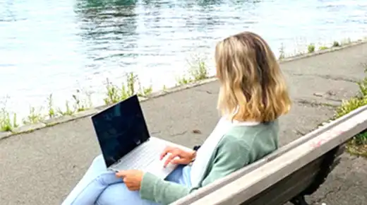 Woman with Laptop on a Bench by the Lake