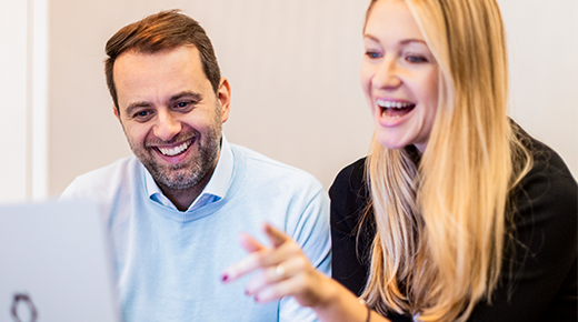 Mann und Frau lachen und schauen sich etwas am Laptop an