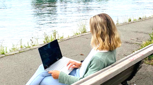 Frau mit Laptop auf einer Bank am See